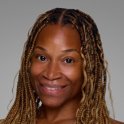 Portrait of a smiling woman with long blonde-brown box braids against a neutral gray background, front view.s