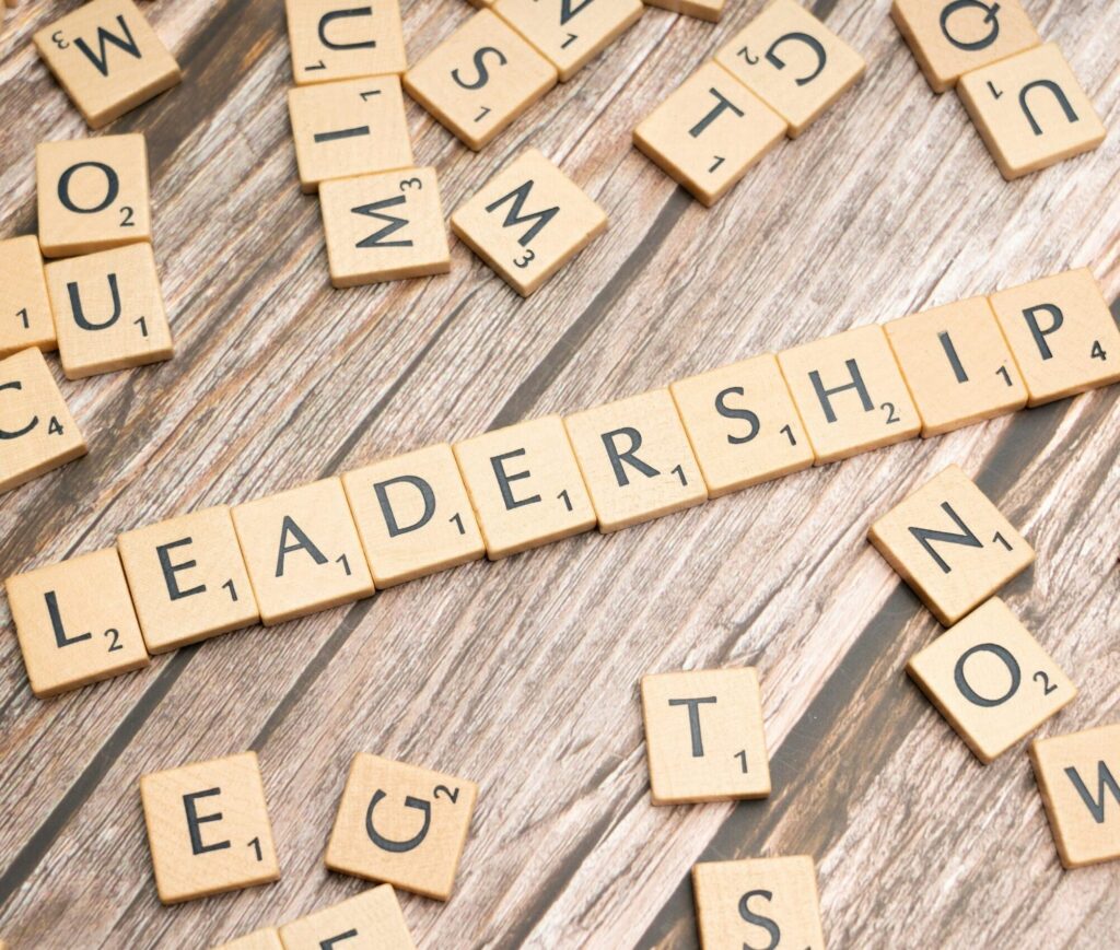 Close-up of Scrabble tiles on a wood surface forming the word'LEADER' with other scattered letters nearby.